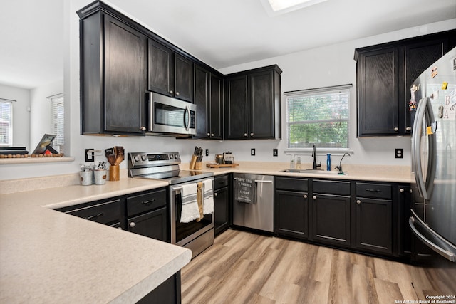 kitchen with stainless steel appliances, light wood-type flooring, sink, and a healthy amount of sunlight