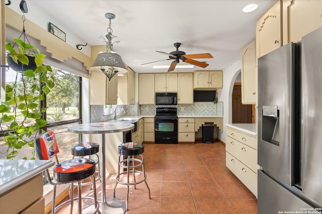 kitchen featuring hanging light fixtures, cream cabinetry, black appliances, tile patterned floors, and ceiling fan