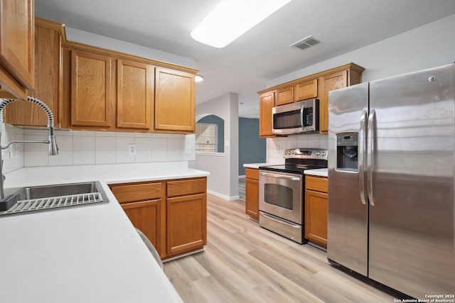 kitchen featuring appliances with stainless steel finishes, light hardwood / wood-style flooring, decorative backsplash, and sink