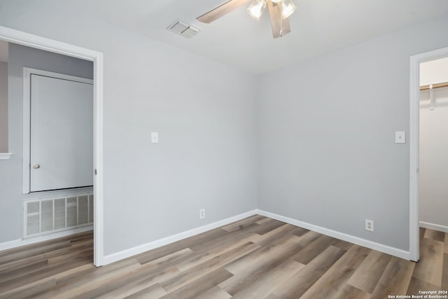 unfurnished bedroom featuring a spacious closet, light hardwood / wood-style flooring, a closet, and ceiling fan