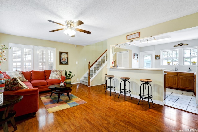 living room with a textured ceiling, ceiling fan, light hardwood / wood-style flooring, and sink