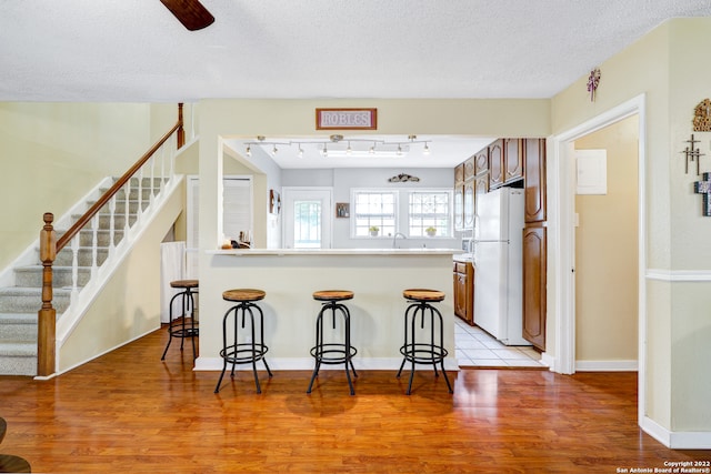 kitchen featuring a textured ceiling, a kitchen bar, light hardwood / wood-style flooring, and white refrigerator