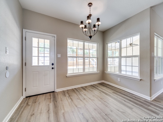 doorway to outside with light wood-type flooring and ceiling fan with notable chandelier