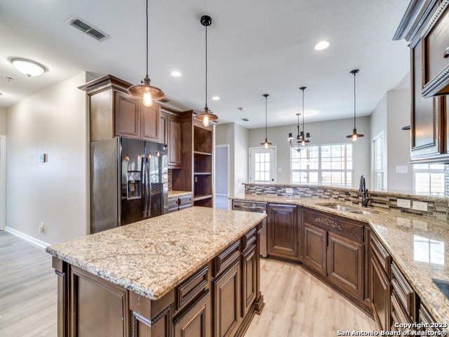 kitchen featuring pendant lighting, a large island, black fridge with ice dispenser, and a healthy amount of sunlight