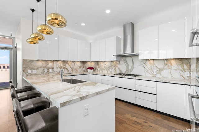 kitchen featuring a kitchen breakfast bar, white cabinetry, wall chimney exhaust hood, decorative light fixtures, and dark hardwood / wood-style floors