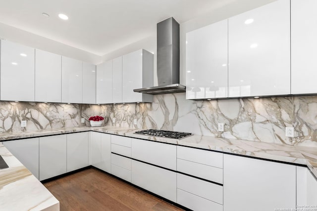 kitchen featuring light stone counters, white cabinets, tasteful backsplash, wall chimney range hood, and dark hardwood / wood-style floors