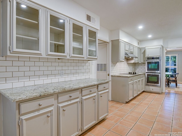 kitchen with light stone countertops, double oven, black electric cooktop, decorative backsplash, and light tile patterned floors