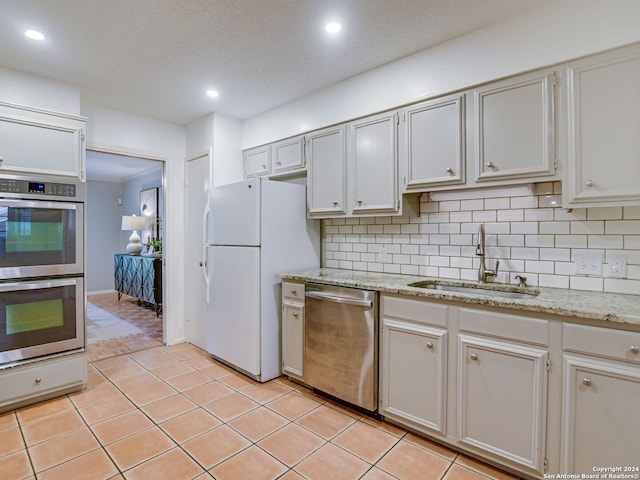 kitchen featuring sink, light tile patterned floors, backsplash, white cabinets, and appliances with stainless steel finishes