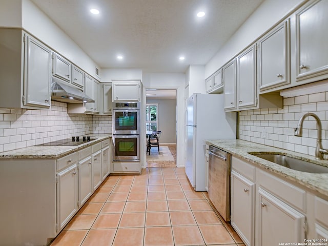 kitchen with light stone countertops, sink, stainless steel appliances, tasteful backsplash, and light tile patterned floors