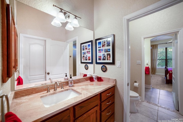 bathroom with vanity, toilet, a textured wall, baseboards, and tile patterned floors