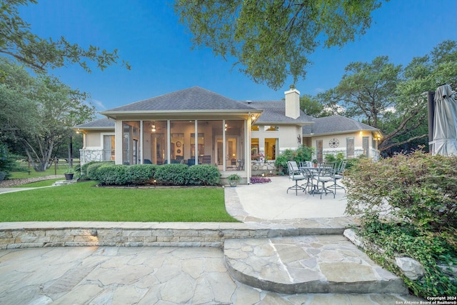 rear view of property featuring a chimney, stucco siding, a sunroom, a patio, and a yard