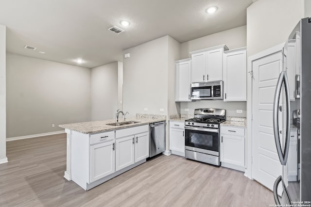 kitchen with light stone countertops, white cabinetry, sink, stainless steel appliances, and kitchen peninsula