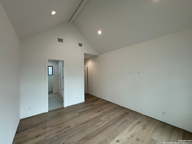 spare room featuring light wood-type flooring, beam ceiling, and high vaulted ceiling