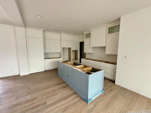 kitchen featuring black electric cooktop, light wood-type flooring, a center island, and white cabinetry