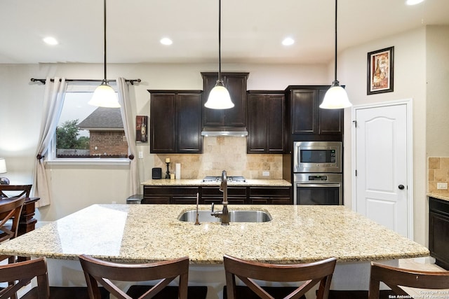 kitchen featuring sink, appliances with stainless steel finishes, hanging light fixtures, an island with sink, and decorative backsplash