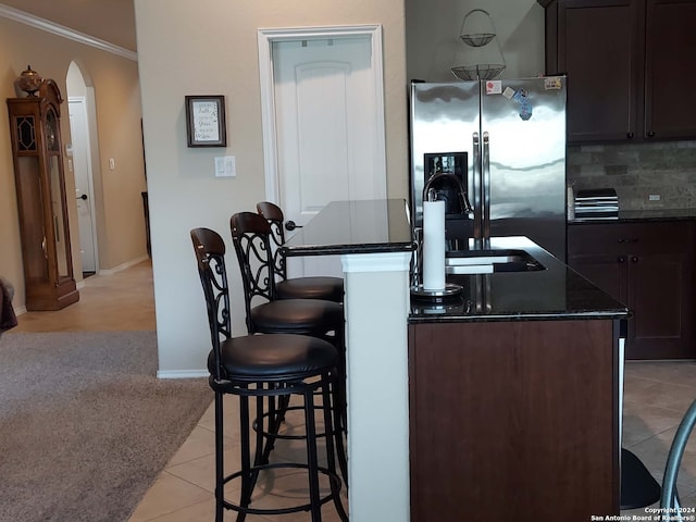 kitchen with a breakfast bar, dark brown cabinetry, light tile patterned floors, a center island with sink, and stainless steel fridge with ice dispenser