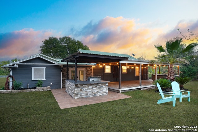 back house at dusk featuring a lawn, exterior kitchen, and a patio area