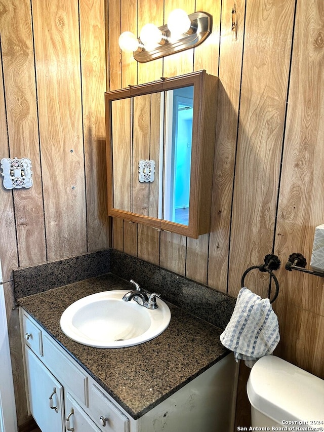 bathroom featuring vanity, wooden walls, and toilet