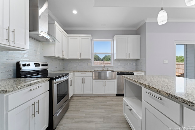 kitchen with appliances with stainless steel finishes, wall chimney exhaust hood, white cabinets, and a wealth of natural light