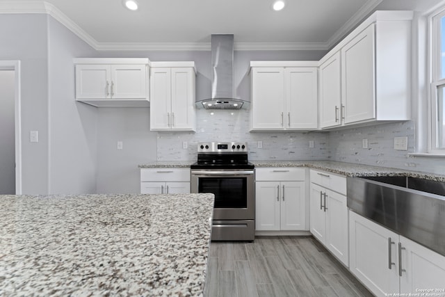 kitchen featuring wall chimney range hood, white cabinetry, stainless steel range with electric cooktop, light stone countertops, and crown molding