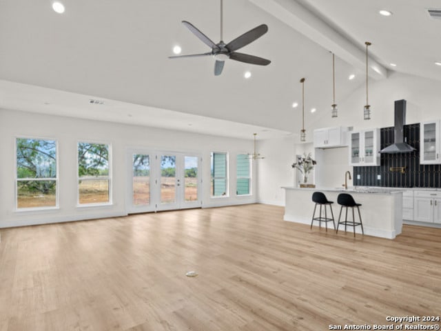 unfurnished living room with beamed ceiling, ceiling fan, light wood-type flooring, and high vaulted ceiling