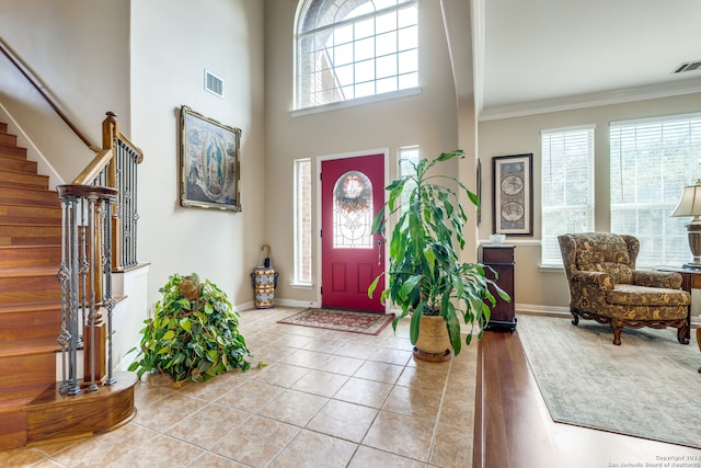 foyer featuring light hardwood / wood-style floors, ornamental molding, and a towering ceiling