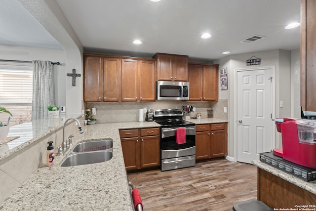 kitchen with stainless steel appliances, light stone counters, light hardwood / wood-style floors, and sink