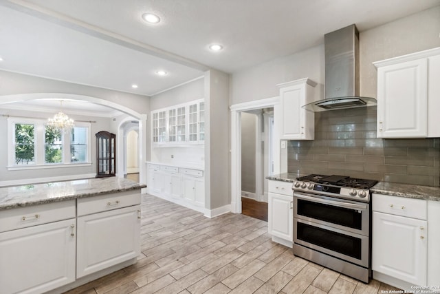 kitchen with light hardwood / wood-style floors, white cabinetry, an inviting chandelier, double oven range, and wall chimney range hood