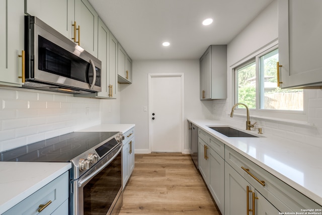 kitchen with appliances with stainless steel finishes, backsplash, light wood-type flooring, and sink