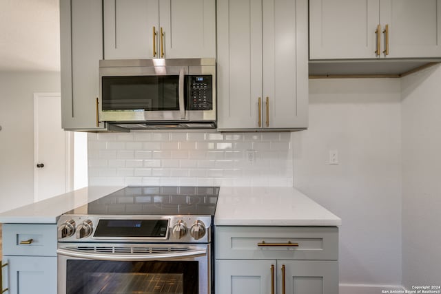 kitchen featuring decorative backsplash, stainless steel appliances, light stone counters, and gray cabinets