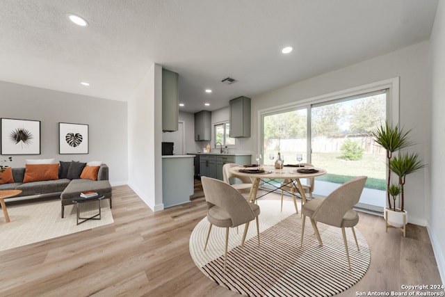 dining area with a textured ceiling, sink, and light hardwood / wood-style flooring