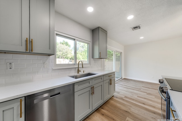 kitchen featuring sink, gray cabinetry, light hardwood / wood-style flooring, appliances with stainless steel finishes, and decorative backsplash