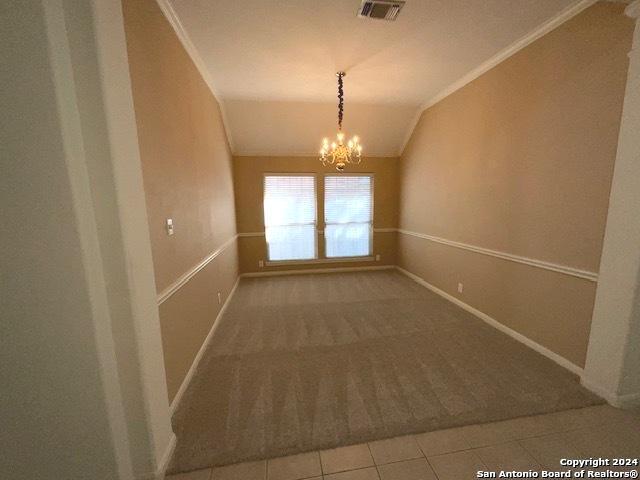 tiled spare room with a notable chandelier, crown molding, and vaulted ceiling