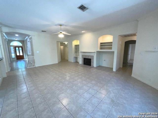 unfurnished living room featuring built in features, a premium fireplace, ceiling fan, and light tile patterned flooring