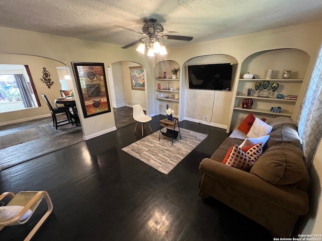 living room featuring ceiling fan, a textured ceiling, built in features, and dark wood-type flooring