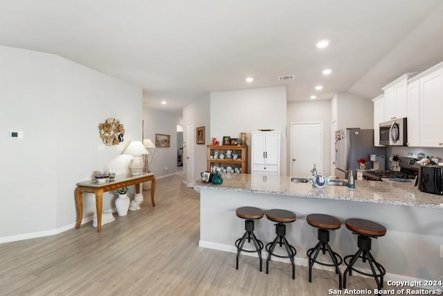 kitchen with light hardwood / wood-style flooring, stainless steel appliances, kitchen peninsula, and white cabinetry