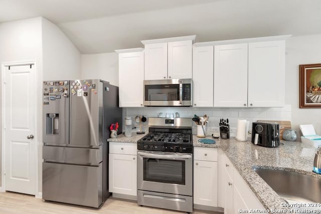 kitchen with white cabinetry, decorative backsplash, stainless steel appliances, light hardwood / wood-style flooring, and light stone countertops