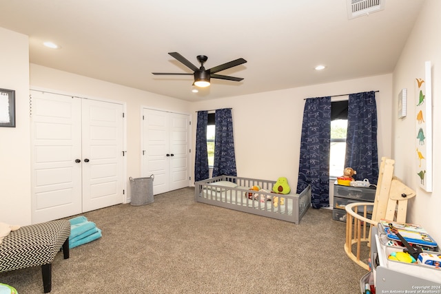 carpeted bedroom with ceiling fan, a nursery area, and multiple closets