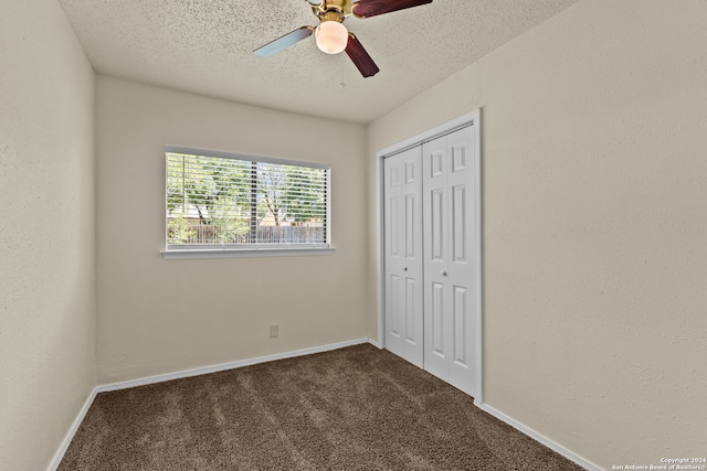 unfurnished bedroom with dark carpet, a textured ceiling, a closet, and ceiling fan