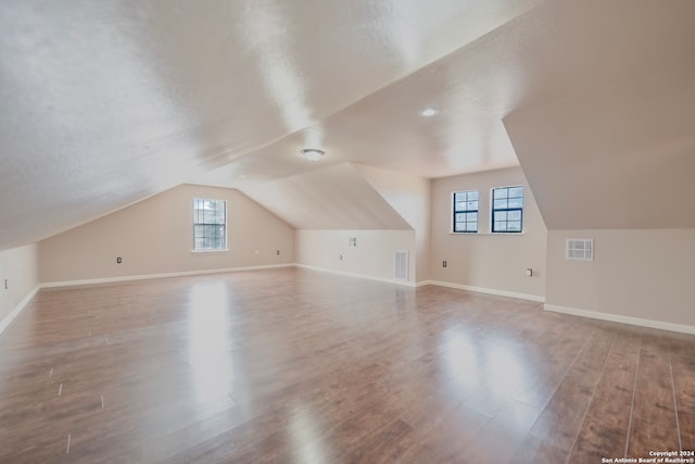 additional living space featuring hardwood / wood-style flooring, lofted ceiling, a textured ceiling, and a wealth of natural light