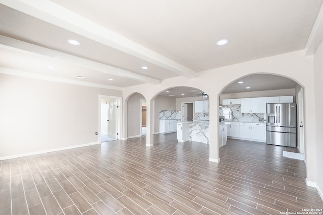 unfurnished living room featuring light wood-type flooring, beam ceiling, and sink