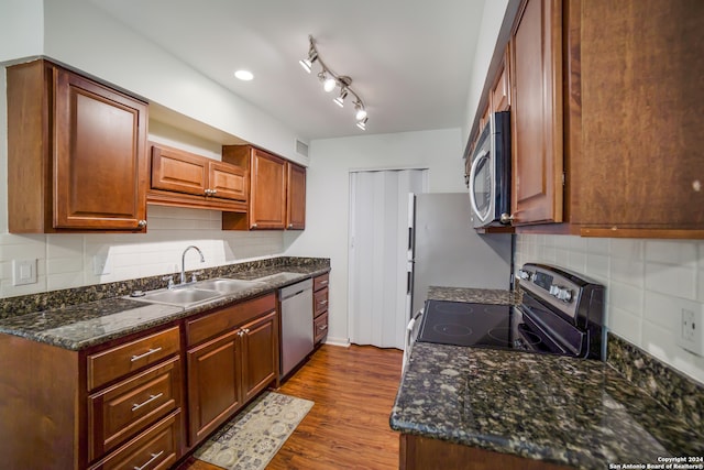 kitchen with dark stone countertops, tasteful backsplash, stainless steel appliances, wood-type flooring, and sink