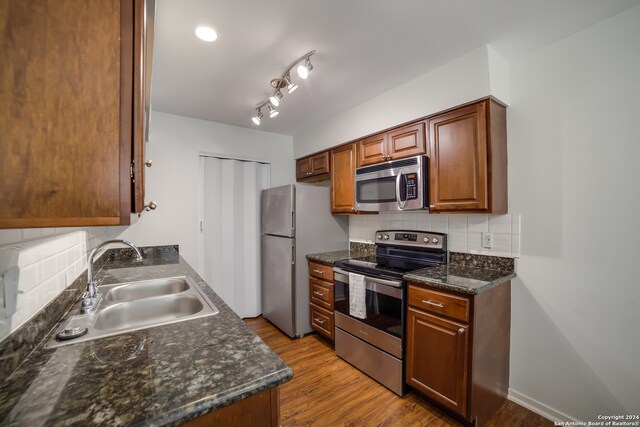 kitchen with backsplash, appliances with stainless steel finishes, light wood-type flooring, and sink