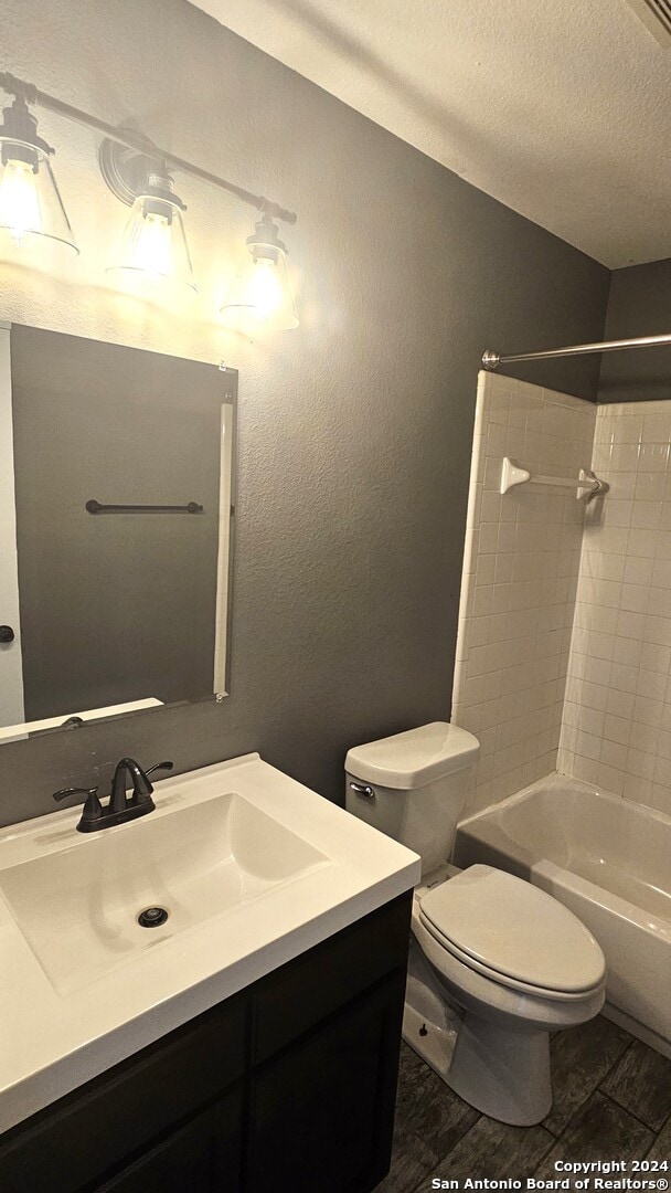 full bathroom featuring vanity, a textured ceiling, tiled shower / bath combo, hardwood / wood-style flooring, and toilet