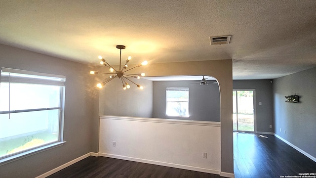 empty room with an inviting chandelier, a textured ceiling, and dark hardwood / wood-style floors