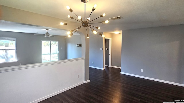 empty room featuring ceiling fan with notable chandelier and dark hardwood / wood-style flooring