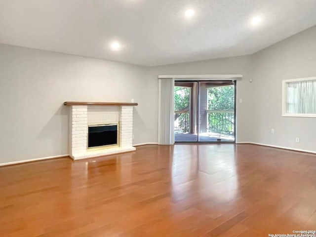 unfurnished living room with a brick fireplace, lofted ceiling, and wood-type flooring