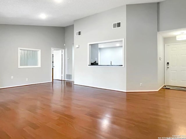 unfurnished living room with a textured ceiling, wood-type flooring, and high vaulted ceiling