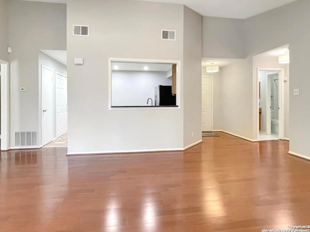 unfurnished living room featuring hardwood / wood-style floors, a towering ceiling, and sink