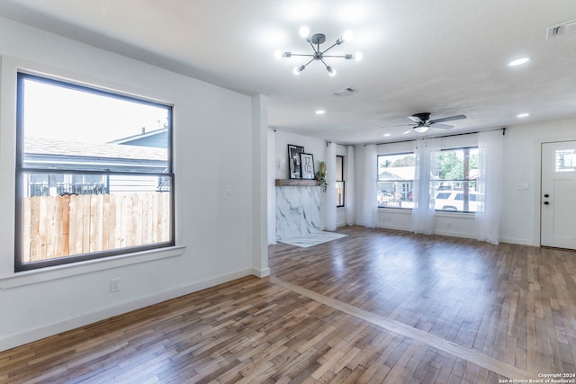 unfurnished living room with ceiling fan with notable chandelier, wood-type flooring, and a textured ceiling